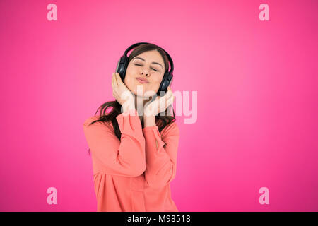 Donna di fronte a parete rosa ascoltando musica sulle cuffie Foto Stock