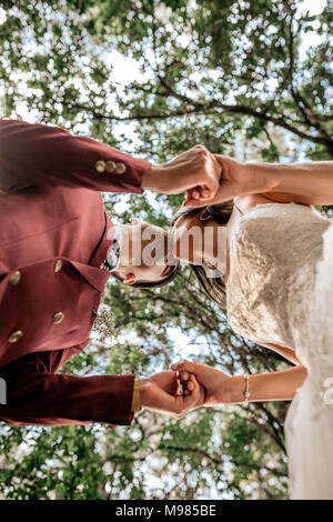 Sposa e lo sposo tenendo le mani e baciare sotto un albero Foto Stock