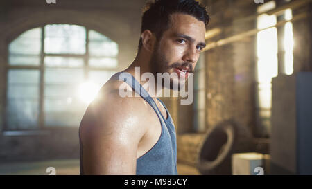 Esaurito l'uomo muscolare cercando nella fotocamera dopo estenuanti palestra di allenamento. Il sudore gocciola dal suo volto, indossa singoletto. Foto Stock