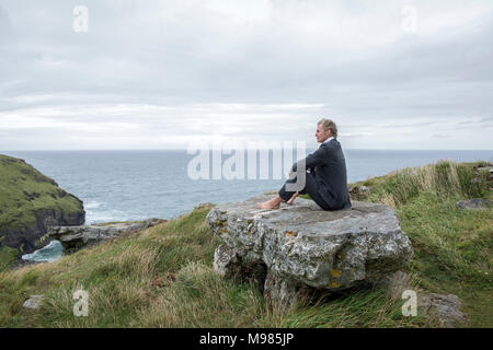 Regno Unito, Cornwall, Tintagel, imprenditore seduto sulla roccia presso la costa cercando di visualizzare Foto Stock