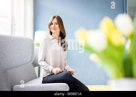 Ritratto di donna sorridente seduto sul divano azienda tablet Foto Stock