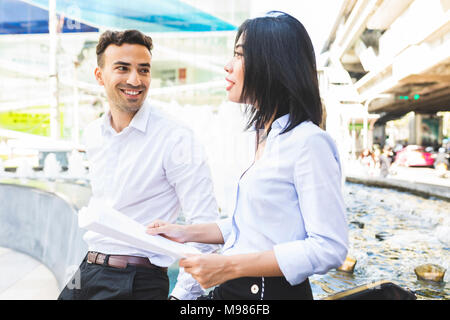 Thailandia, Bangkok, sorridente imprenditore e imprenditrice con documenti parlando in città Foto Stock