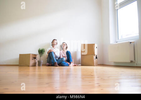 Sorridente Coppia matura seduta sul pavimento nella stanza vuota accanto a scatole di cartone Foto Stock