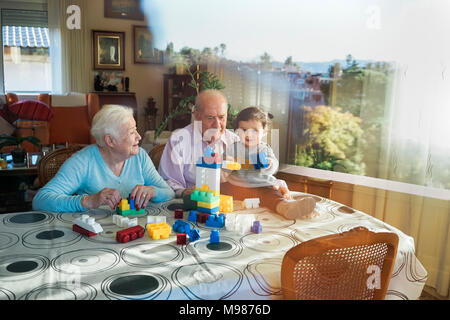 Grande-nonni e baby girl insieme giocando in plastica con mattoni di edificio a casa Foto Stock