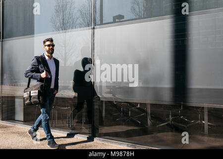 Imprenditore indossando occhiali da sole passeggiando lungo edificio Foto Stock