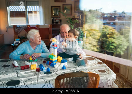 Grande-nonni e baby girl insieme giocando in plastica con mattoni di edificio a casa Foto Stock