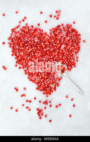 A forma di cuore di semi di melograno su marmo bianco Foto Stock