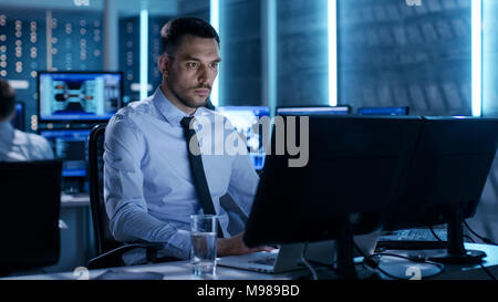 Professional Controller tecnico con i colleghi sulle loro workstation. Sono in Sala di monitoraggio con più monitor che li circondano. Foto Stock