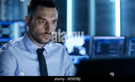 Professional Controller tecnico con i colleghi sulle loro workstation. Sono in Sala di monitoraggio con più monitor che li circondano. Foto Stock