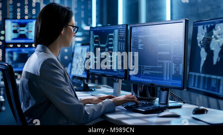 Femmina ingegnere di sistema controlla la procedura operativa. Sullo sfondo i monitor di lavoro visualizza varie informazioni. Foto Stock