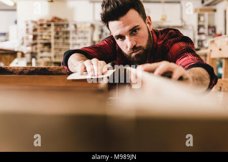 L'uomo il trattamento del legno in officina con della carta vetrata Foto Stock