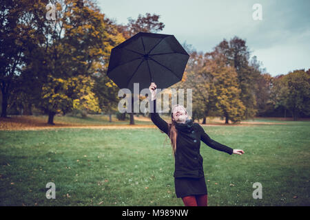 Giovane donna ballando con ombrello in parco autunnali Foto Stock