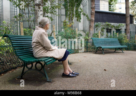 Lonely vecchia signora seduta su una panchina nel parco, guardando lontano, Parigi Foto Stock