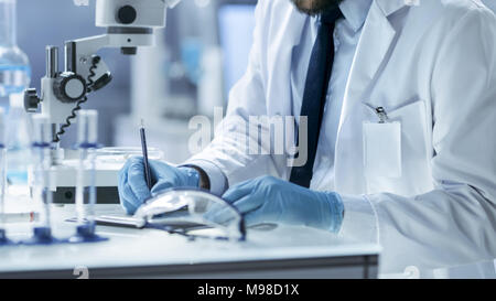 Research Scientist scrive all esperimento osservazioni. Sta lavorando nel laboratorio moderno. Foto Stock