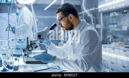 In un moderno laboratorio scienziato conduce esperimenti con materiali organici. Lui sta cercando in un microscopio. Foto Stock