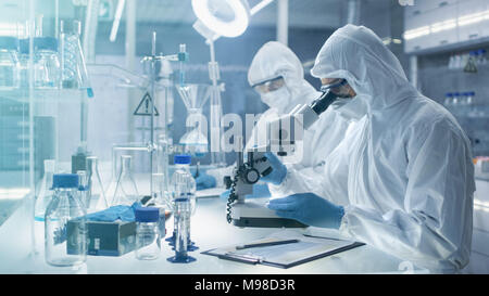 In un luogo sicuro ad alto livello gli scienziati del laboratorio in una tuta da lavoro a condurre una ricerca. Farmacia campioni di regola una piastra Petri con pinze e poi Examins Foto Stock