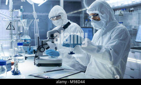 In un luogo sicuro ad alto livello gli scienziati del laboratorio in una tuta da lavoro a condurre una ricerca. Farmacia regola i campioni e il suo collega scrive i risultati. Foto Stock