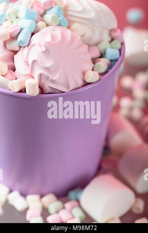 Violetta secchio con vari marshmallows su uno sfondo di colore rosa. Foto Stock