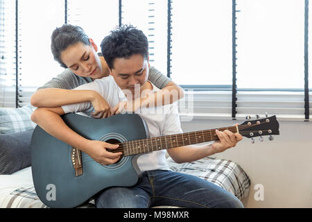 Coppie giovani suonare la chitarra tohether nella camera da letto di casa contemporanea per lo stile di vita moderno concetto Foto Stock