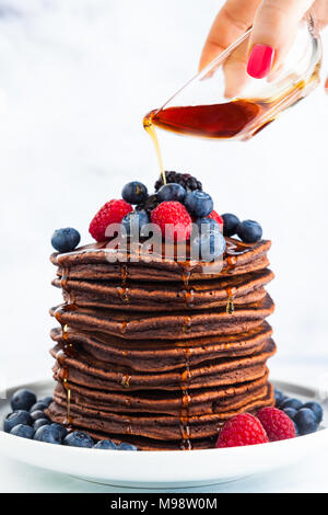 Scorre sciroppo di acero su una pila di pancake al cioccolato con frutti di bosco freschi. mattina colazione sana Foto Stock