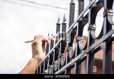 Mano con verniciatura a pennello di recinzione metallica Foto Stock