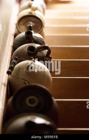 Una fila di antiche ceramiche brocche allineate su una scala, con il sole che crea un effetto di ombre sui gradini in legno. Foto Stock