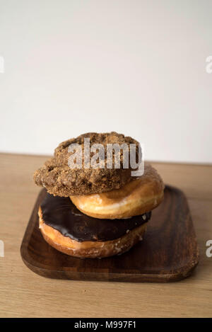 Le ciambelle impilati su un piatto di legno davanti a uno sfondo luminoso Foto Stock