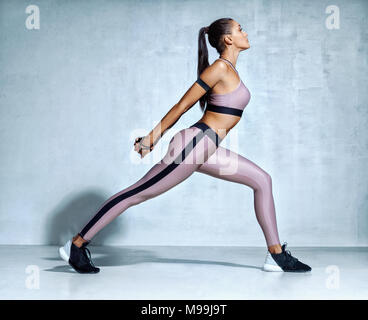 In fase di riscaldamento prima del training. Sportivo da donna in abbigliamento sportivo gambe di stiro su sfondo grigio. Forza e motivazioni. Vista laterale Foto Stock