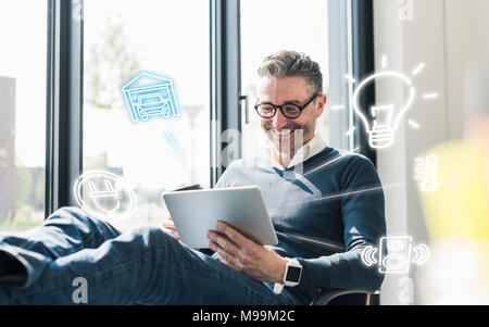 Uomo seduto in ufficio utilizzando la tavoletta digitale per controllo remoto il suo smart home Foto Stock