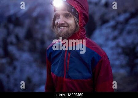 Ritratto di uomo sorridente indossando il proiettore al tramonto in montagna Foto Stock