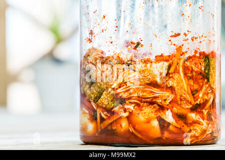 Contenitore di vetro jar closeup di fresco peperone piccante in casa il cavolo fermentato kimchi coreano con rosso scuro, succo di verdura Foto Stock