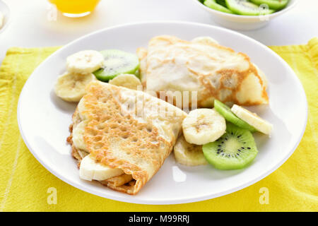 Crepes con banana e kiwi fette sulla piastra bianca. Vista ravvicinata Foto Stock