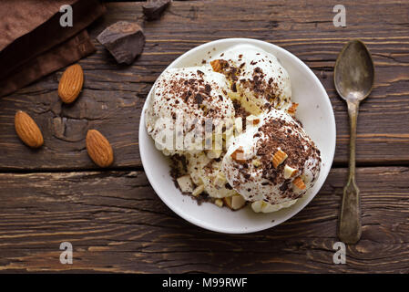 Gelato al cioccolato con noci in vaso su sfondo di legno. Freddo dessert estivo. Vista superiore, laici piatta Foto Stock