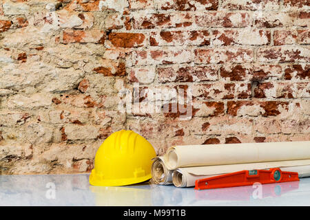 Costruzione di edifici: casco di sicurezza e disegni di progetto su un muro di mattoni sfondo Foto Stock