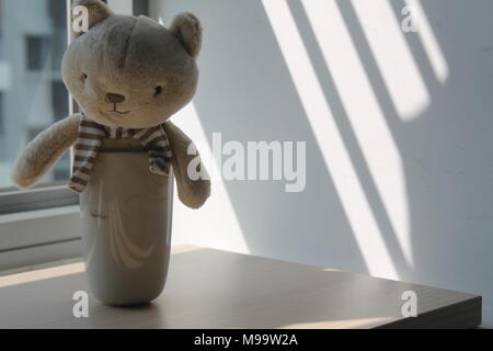 Kitten giocattolo con tazza di seduta dalla finestra di ombre Foto Stock