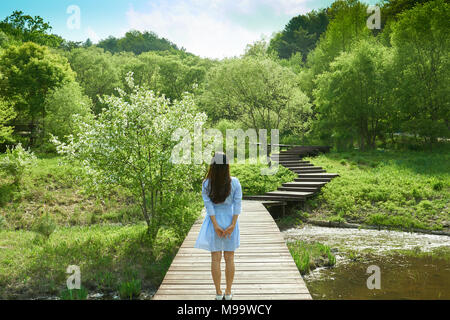 Bellissima vista della natura con la donna in blu mantello rivolta verso il cielo ricordando le memorie del passato su un ponte che va oltre un piccolo stagno. Foto Stock
