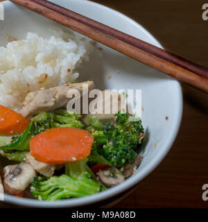 Pollo stir fry servito in tazza bianca con riso, bastoncini, cena angolo di visione - Cucina cinese Foto Stock