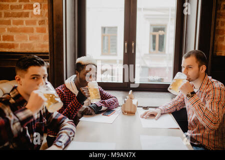 Sorridenti amici maschi tintinnanti con boccali da birra in pub Foto Stock