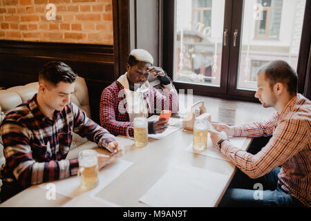 Multirazziale amici bere birra nei pub in seduta il loro telefono. Foto Stock