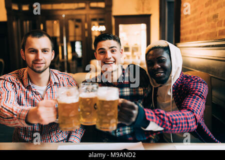 Happy amici maschi a bere birra e tintinnanti bicchieri al bar o pub Foto Stock