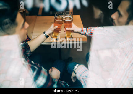 Multirazziale vecchi amici si incontrano in un pub e bere birra e parlando e divertirsi vista attraverso la finestra. Foto Stock