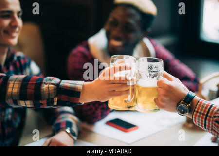 Sorridenti amici maschi tintinnanti con boccali da birra in pub Foto Stock