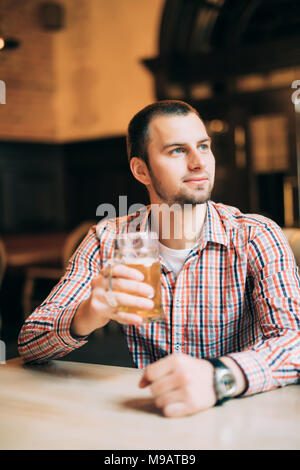 Bel giovane bere birra chiara in un pub. Foto Stock