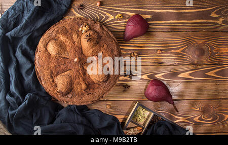 Torta al cioccolato con le pere stufati nel vino rosso, nocciole, noci su sfondo di legno. Dolce tradizionale. Vista dall'alto. Copia dello spazio. Foto Stock