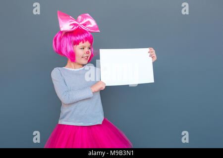 Bellissima bambina in costume da clown holding scrivania bianca. Studio shot, isolata su uno sfondo grigio Foto Stock