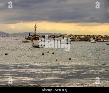 Piccole barche da pesca ormeggiate nella piccola baia in Grecia KINI .Silhouette di un pescatore alla fine del molo al golden ora. Stock Photo. Foto Stock