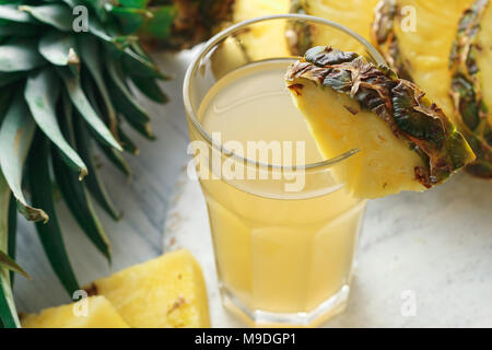 Ananas spremuta fresca in vetro su un tavolo in legno su cemento grigio sfondo Foto Stock