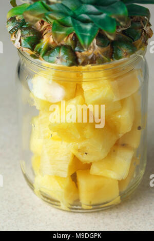 Fresh succoso e pezzi di ananas in un vasetto di vetro sul tavolo di cucina contro il grigio Sfondo rile Foto Stock