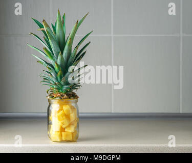 Fresh succoso e pezzi di ananas in un vasetto di vetro sul tavolo di cucina contro il grigio Sfondo rile Foto Stock