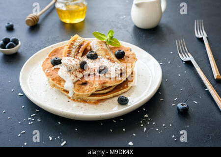 Frittelle di avena con yogurt greco, arrosto di banana, mirtilli e cannella sulla piastra bianca Foto Stock